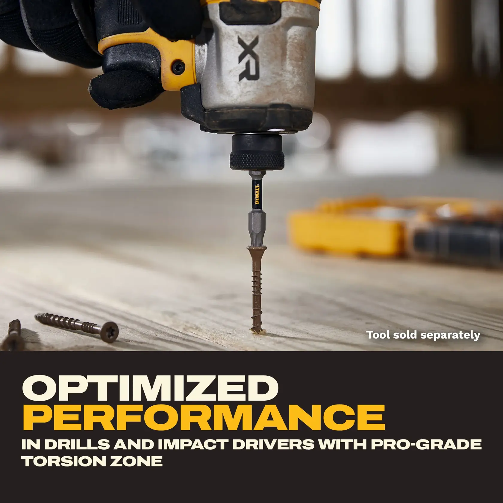 A close-up of a hand wearing a glove using a DEWALT XR power tool to drive a screw into a wooden surface. The text reads: 'Optimized performance in drills and impact drivers with pro-grade torsion zone.' The tool is sold separately. A yellow toolbox is blurred in the background.