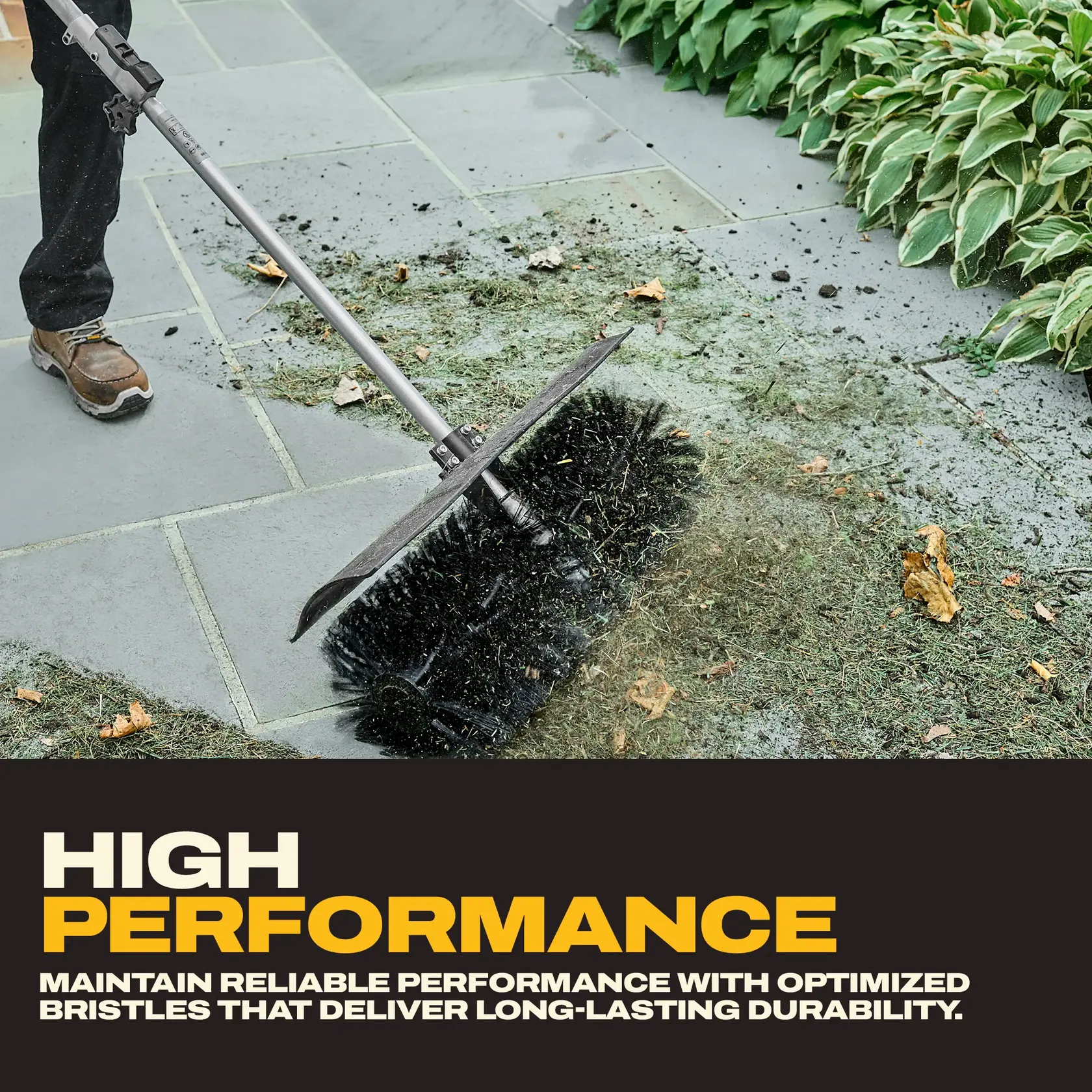 A person uses a DEWALT outdoor power broom with bristles to clean leaves and debris from a stone walkway.