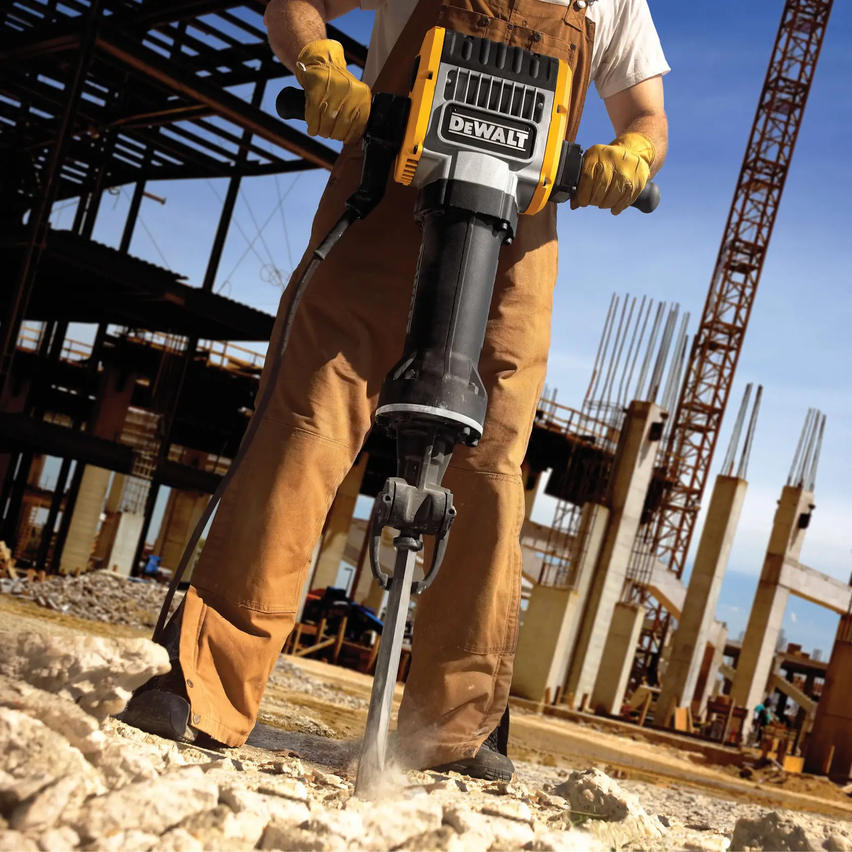 A construction worker operating a DEWALT jackhammer connected to a portable DEWALT generator, breaking up concrete at a demolition site.