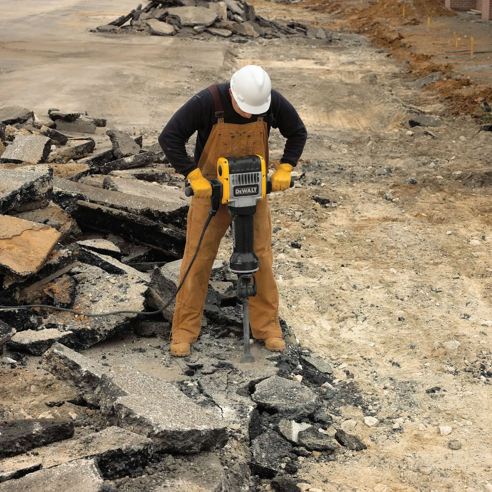 A worker wearing a hard hat and gloves uses a DEWALT jackhammer to break up concrete or asphalt on a construction site.