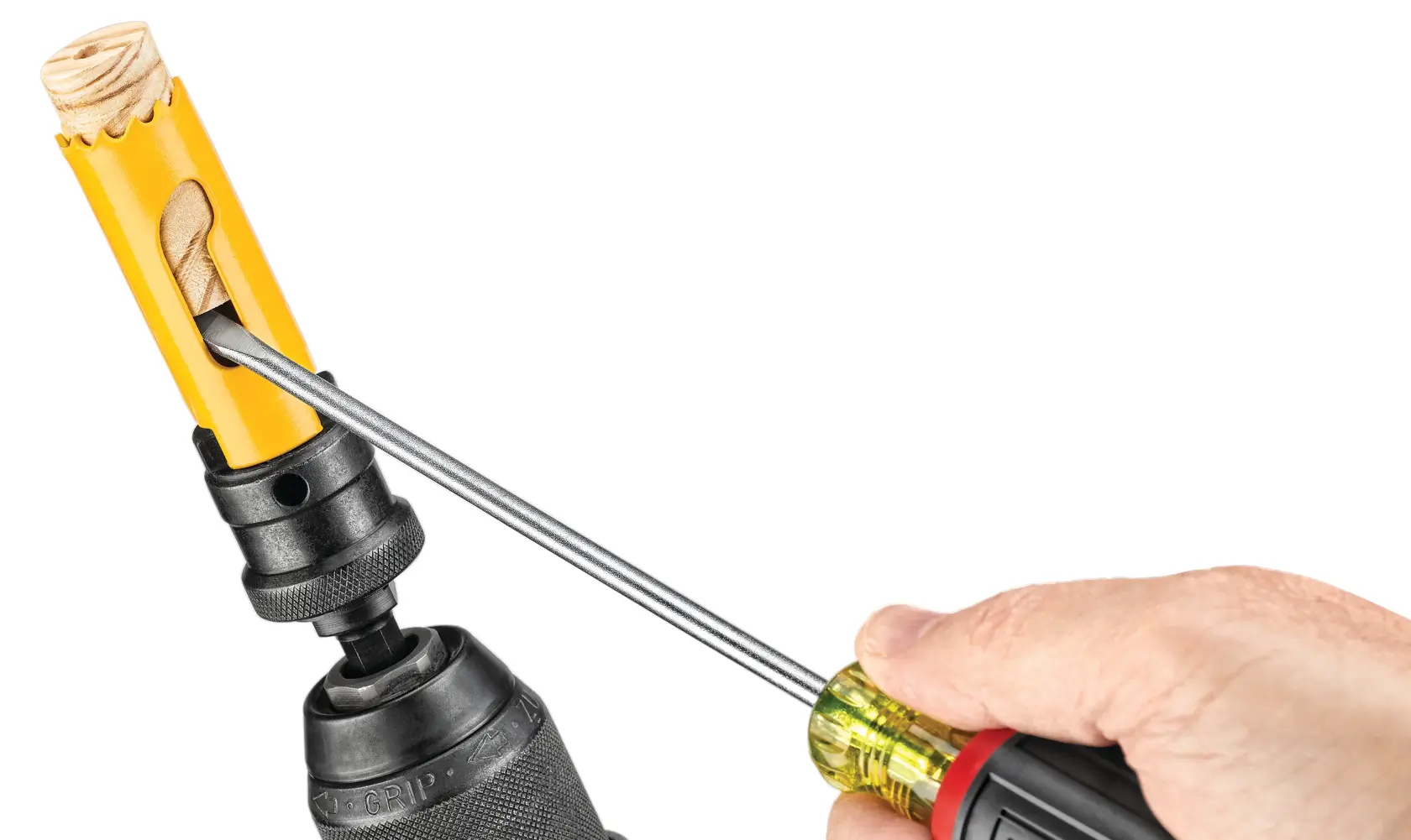A close-up image showing a hand using a screwdriver to remove a wooden plug from a yellow hole saw attachment connected to a drill.