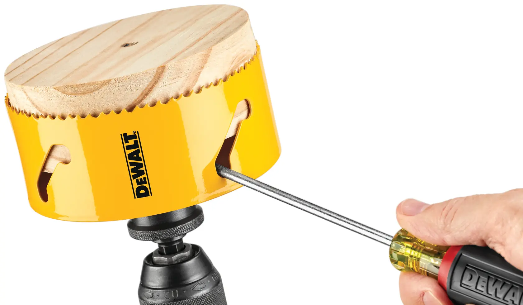 A hand uses a DEWALT screwdriver to remove a wooden disk from a yellow DEWALT hole saw attached to a drill.