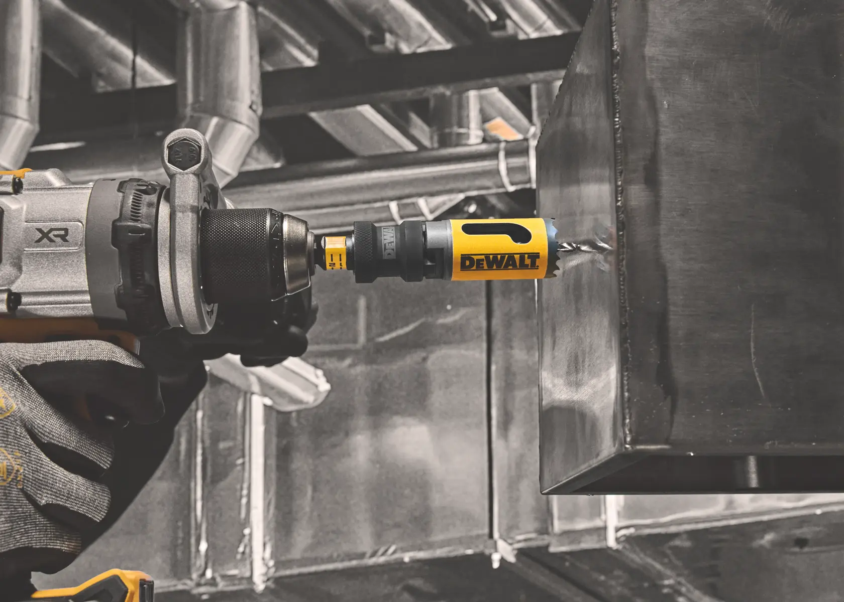 A DEWALT drill with a hole saw attachment drills into a metal surface in an industrial setting.