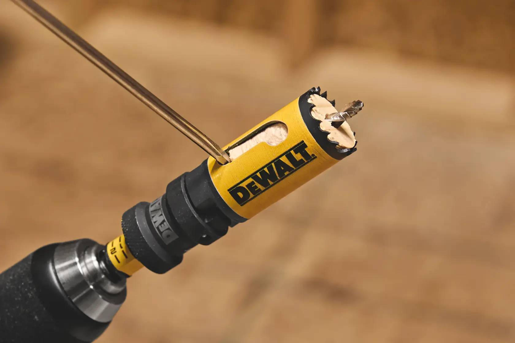 DEWALT yellow hole saw attached to a drill, cutting through wood with visible wood chips.