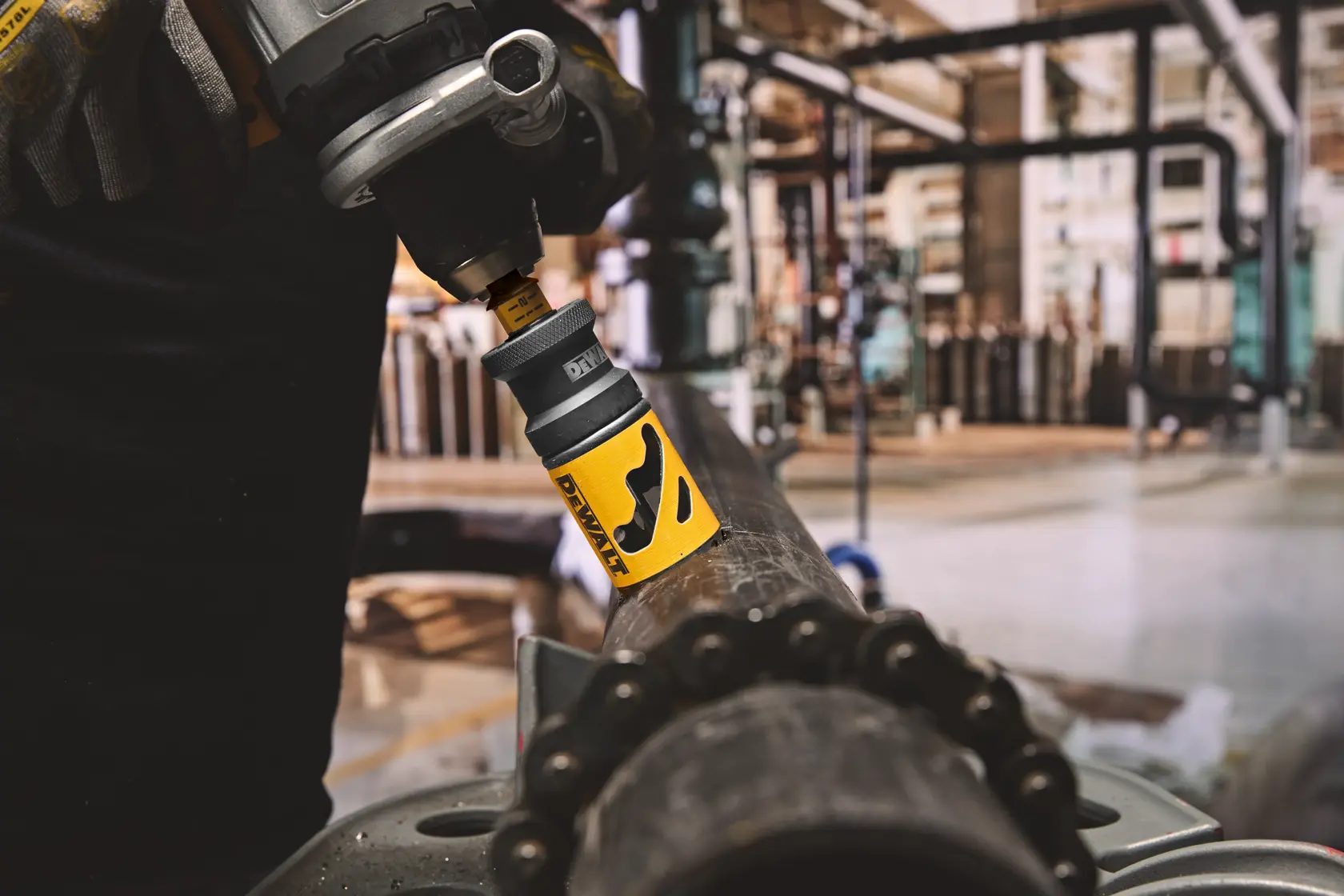 DEWALT hole saw attached to a drill cuts through a metal pipe in an industrial workshop setting.