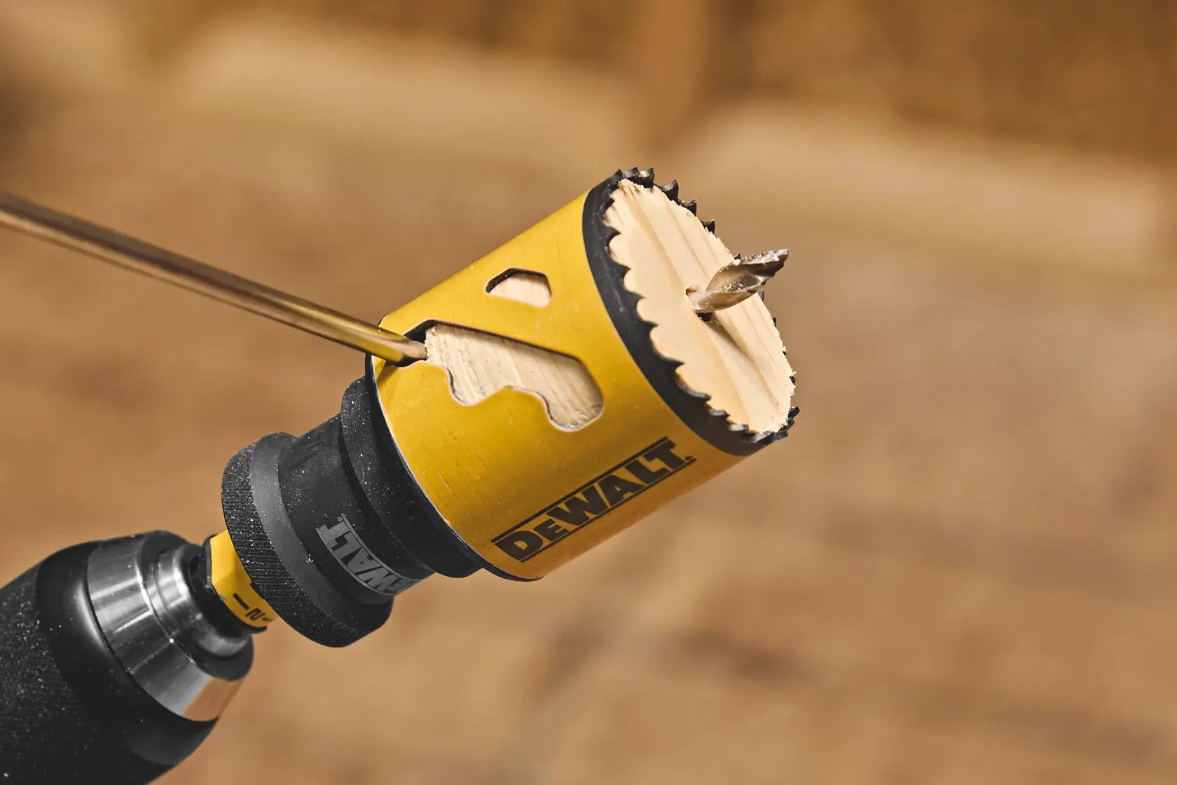 Close-up of a DEWALT hole saw attached to a drill, cutting into wood.