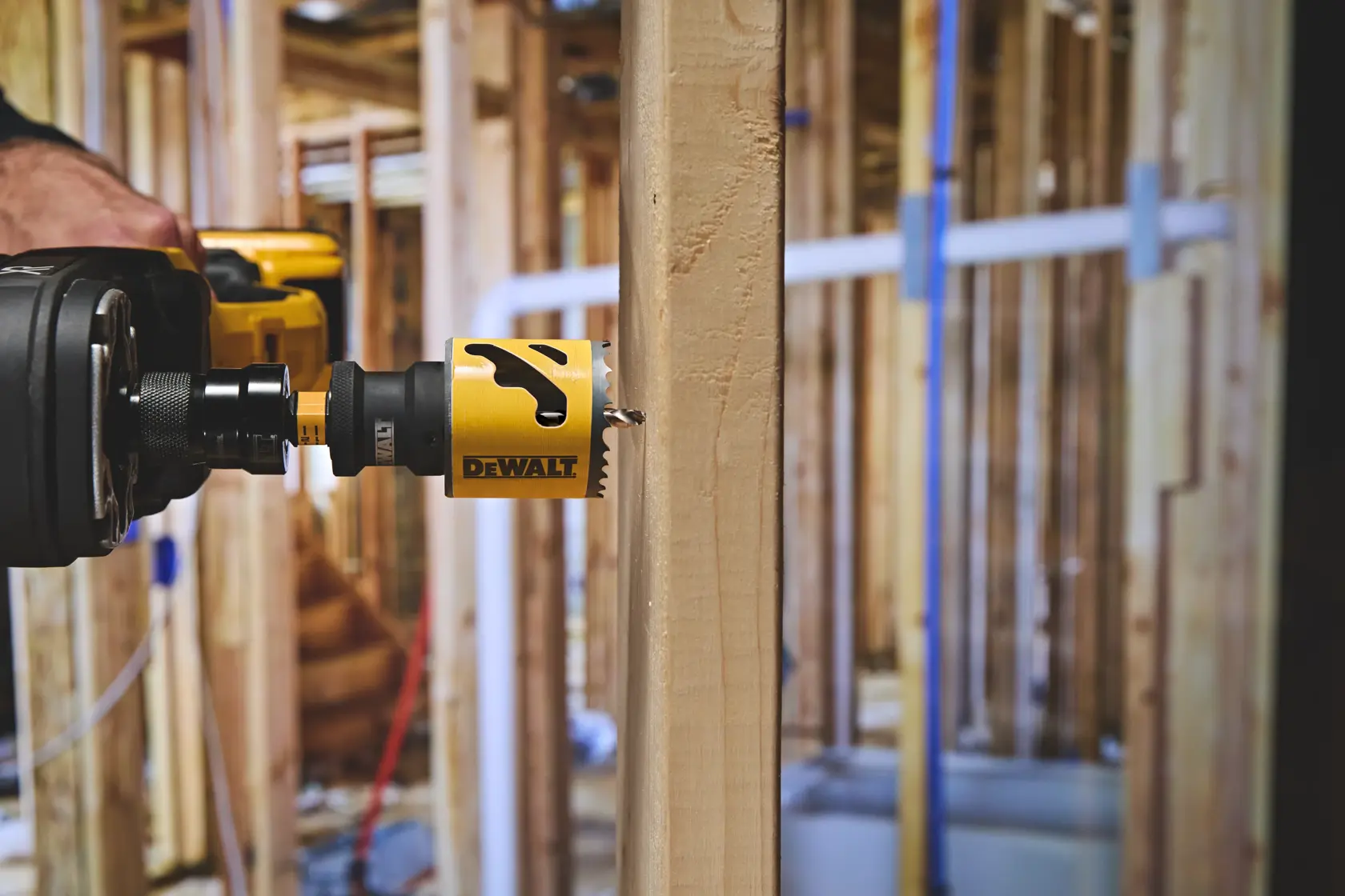 DEWALT power drill with hole saw cutting through wooden stud at a construction site.