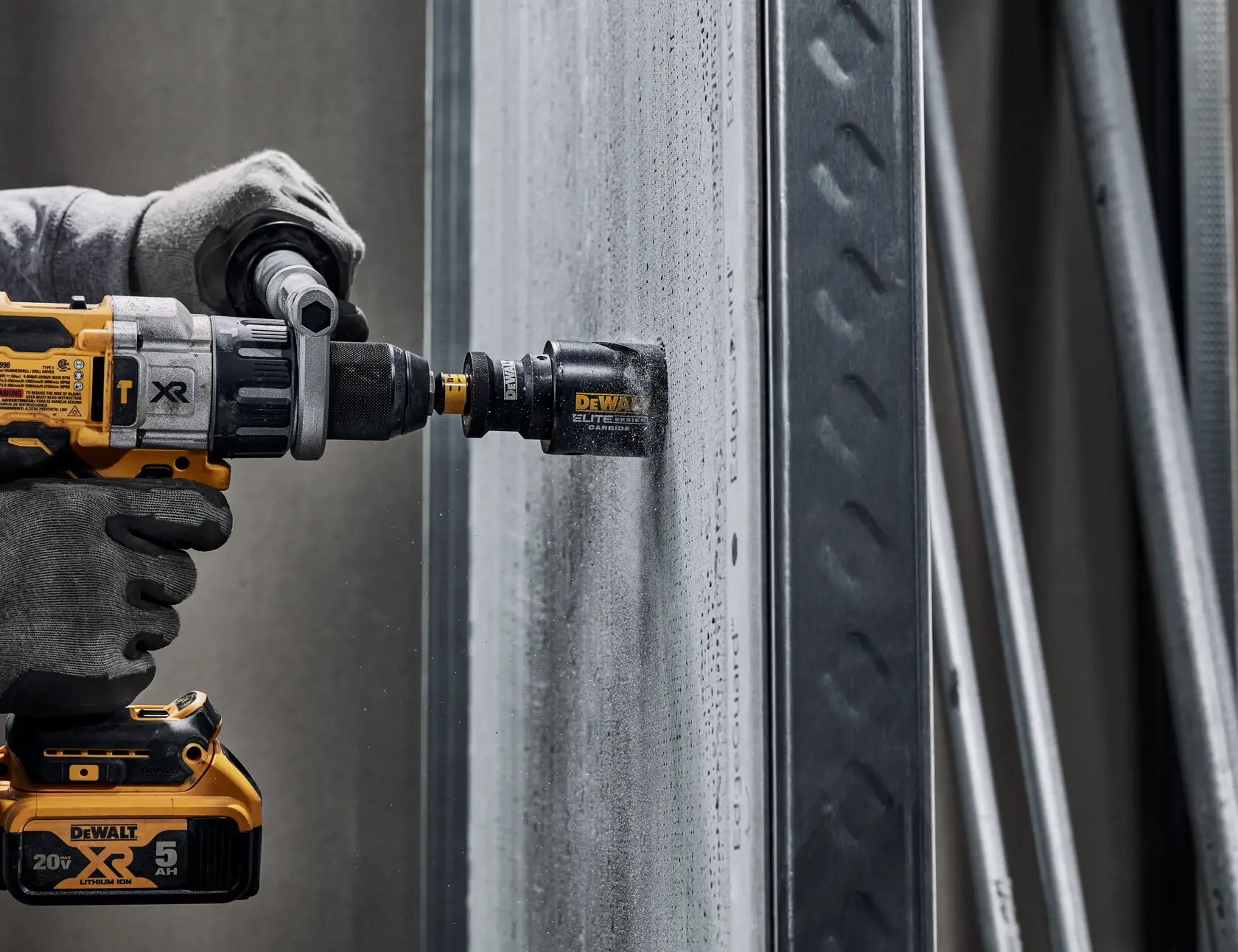 A gloved hand uses a DEWALT cordless drill fitted with a hole saw attachment to bore into a concrete wall. The DEWALT branding and specifications are visible on the tool.