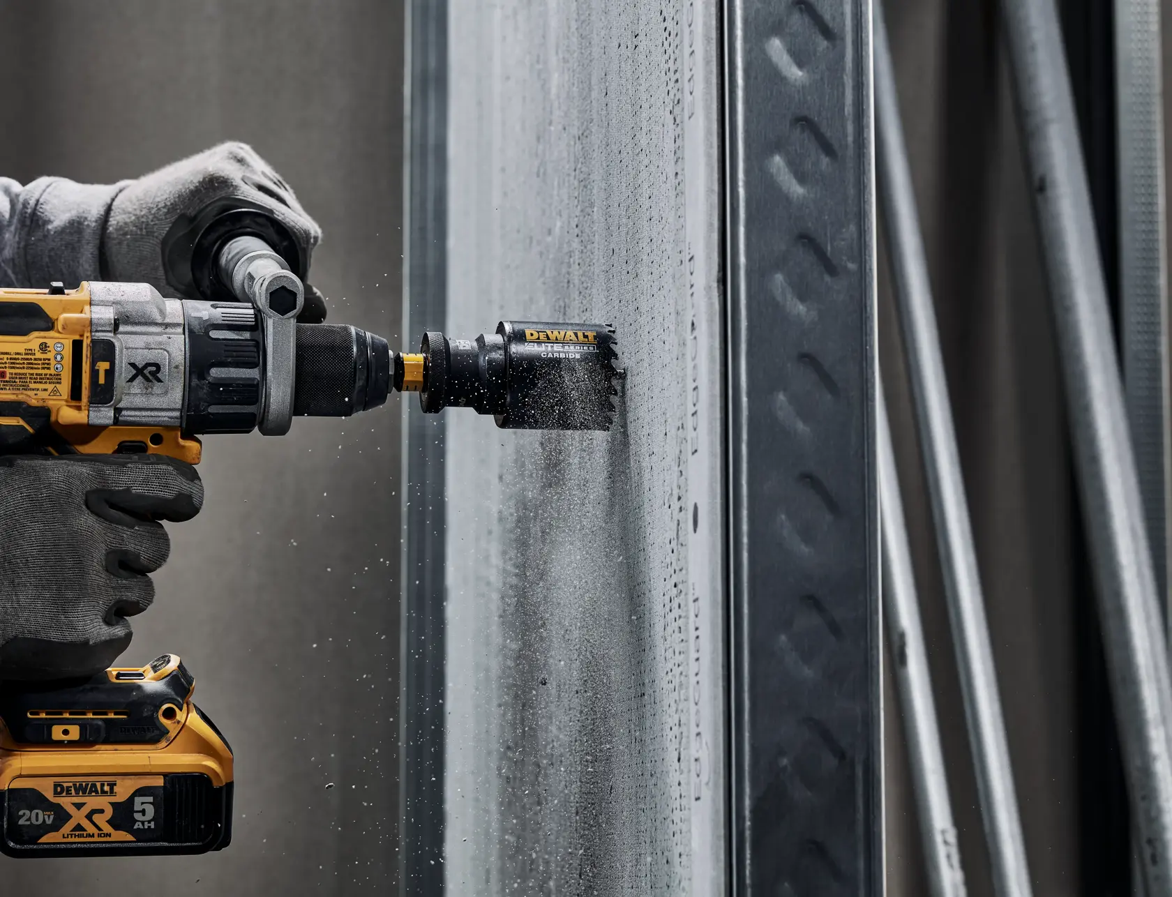 A close-up of a person using a DEWALT cordless power drill with a hole saw attachment to drill into a concrete or cement board wall. The person is wearing work gloves and dust is visible from the drilling process.