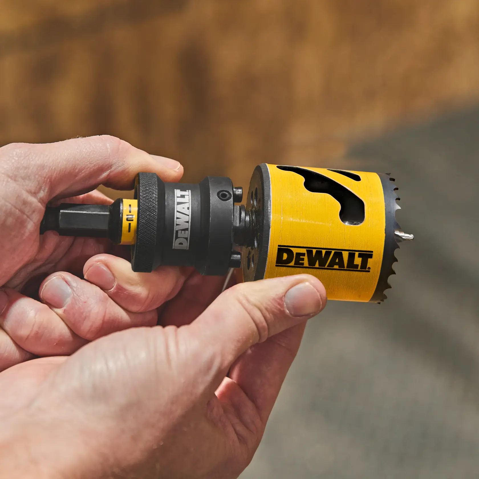 Hands holding a DEWALT yellow hole saw drill bit with sharp teeth, used for cutting holes in materials.