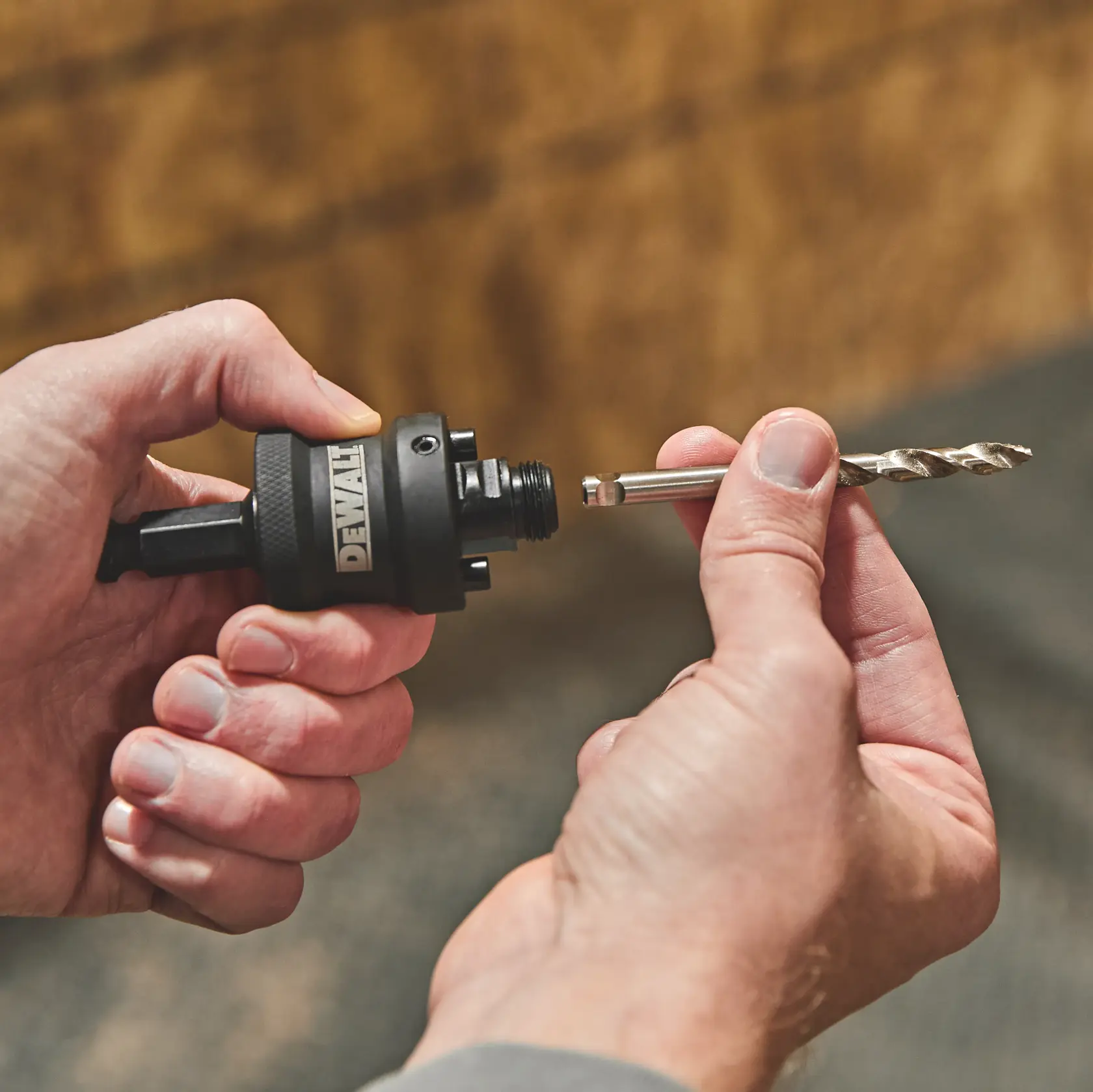 Hands holding a DEWALT drill chuck and a drill bit, preparing to insert the bit into the chuck.
