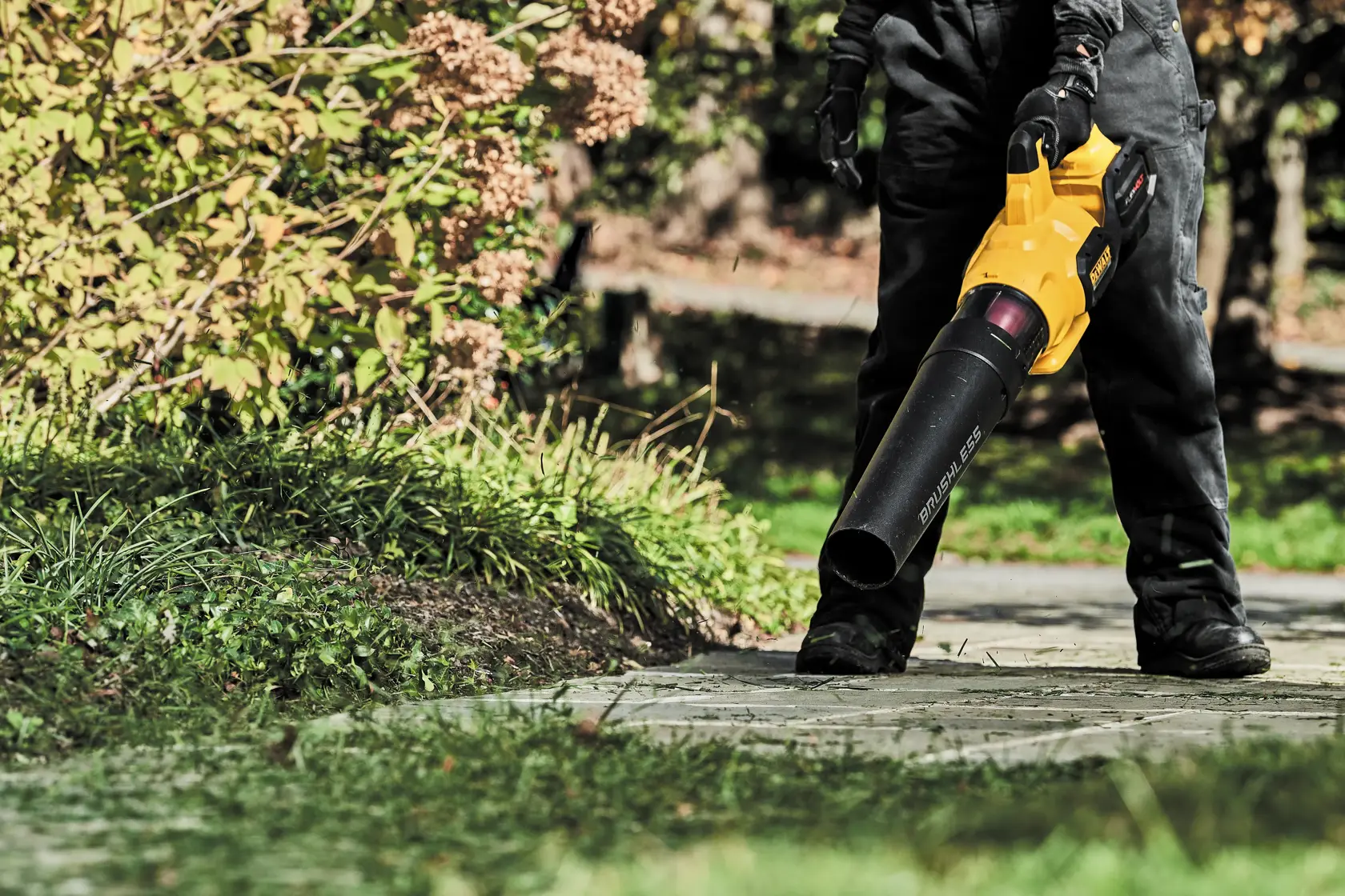 FLEXVOLT Brushless Cordless Handheld Axial Blower being used by a person to clear leaves off  ground in a lawn