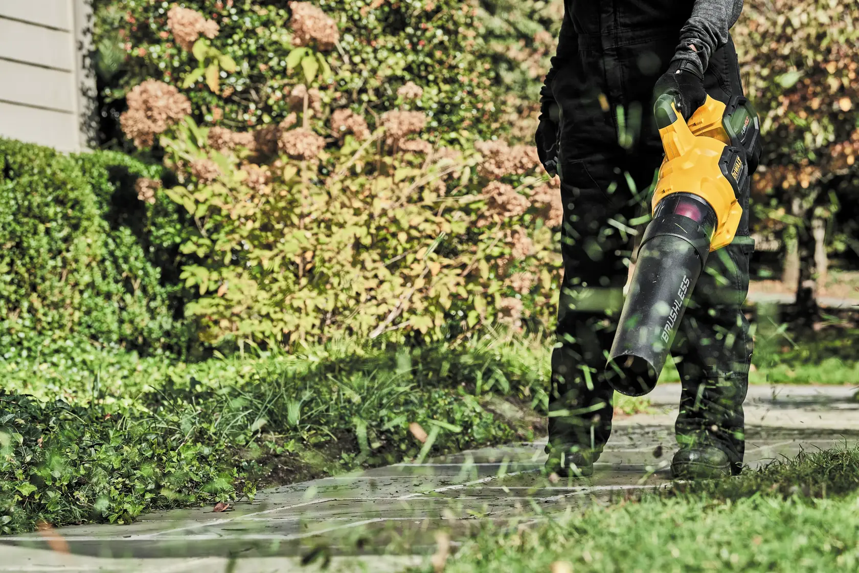 FLEXVOLT Brushless Cordless Handheld Axial Blower being used by a person to clear away grass blades