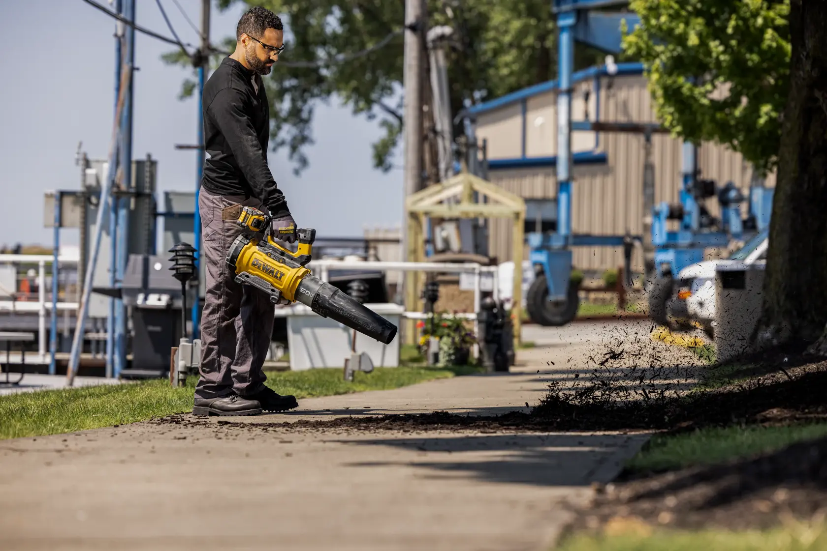 DEWALT 60V Blower being used to blow mulch by a man at an industrial location.