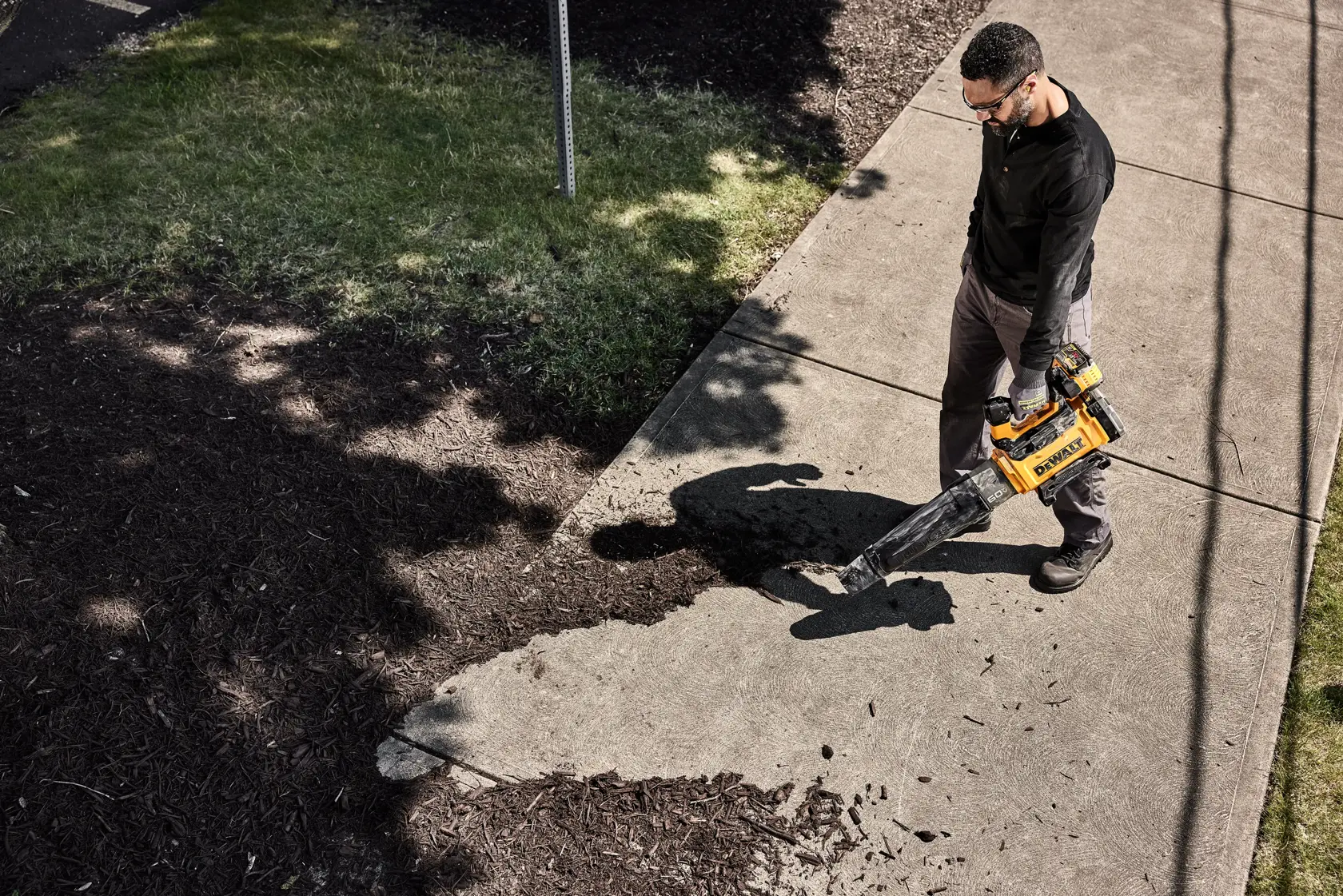 DEWALT 60V* Blower being used to blow mulch on a sidewalk by a man viewed from above. 