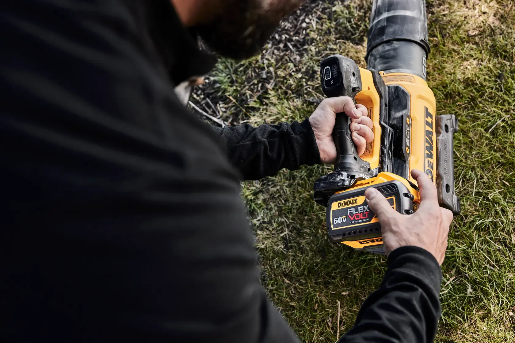 A person using a DEWALT 60V FLEXVOLT cordless leaf blower, holding the tool while standing on grass.