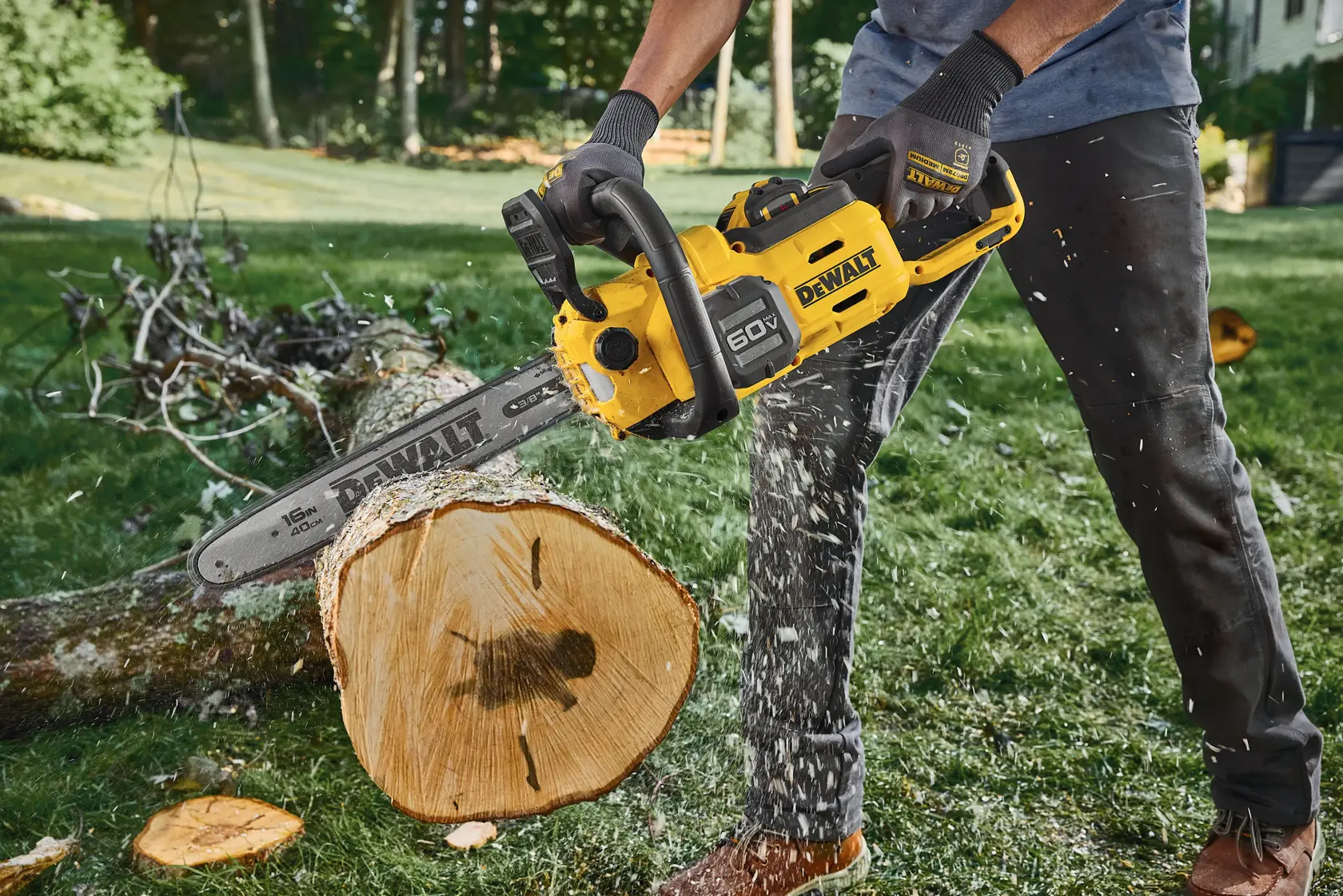 Person using a DEWALT chainsaw to cut a log outdoors, wood chips flying, grassy area in background.
