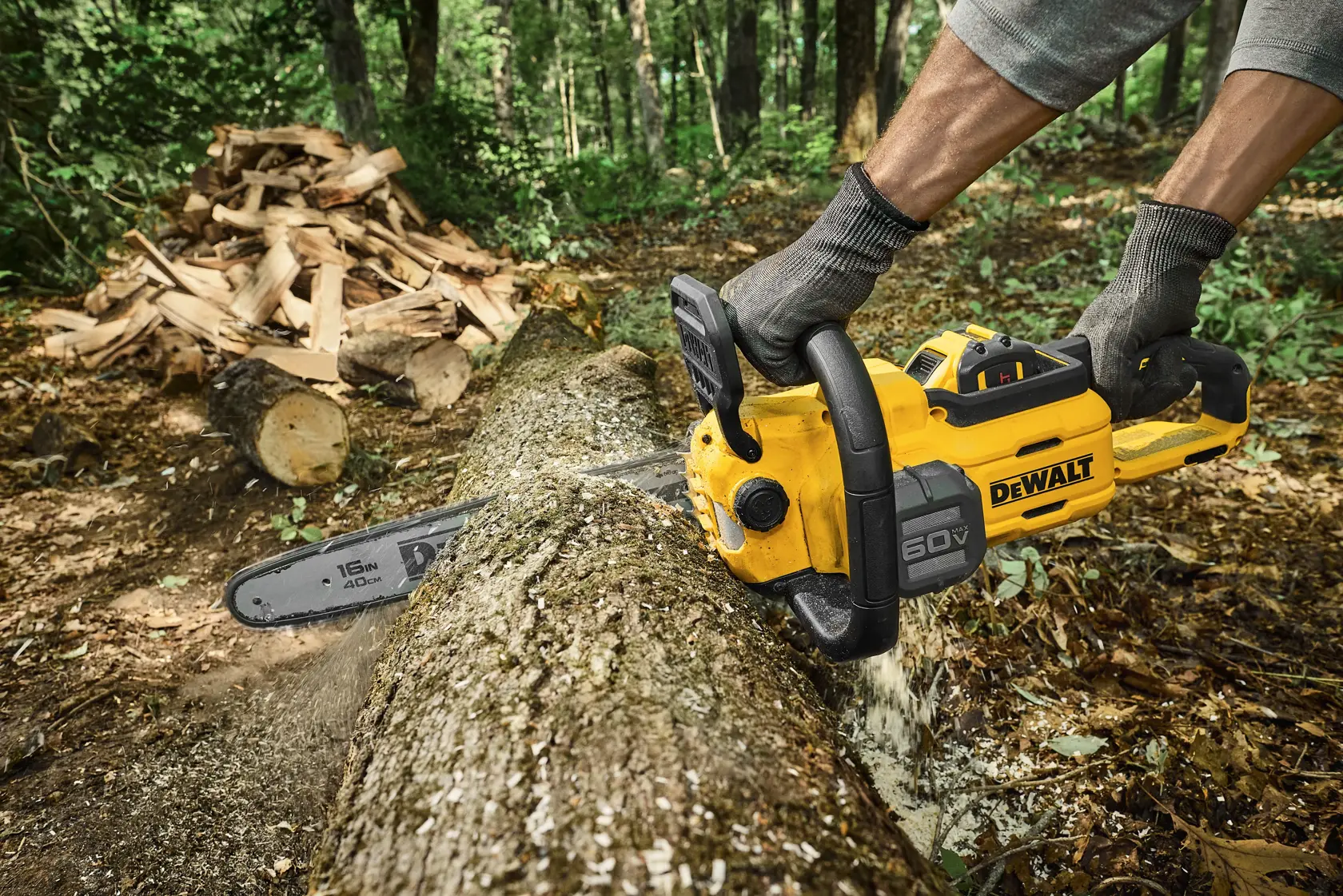 Person using a DEWALT 60V chainsaw to cut a log in a forest with stacked firewood in the background.
