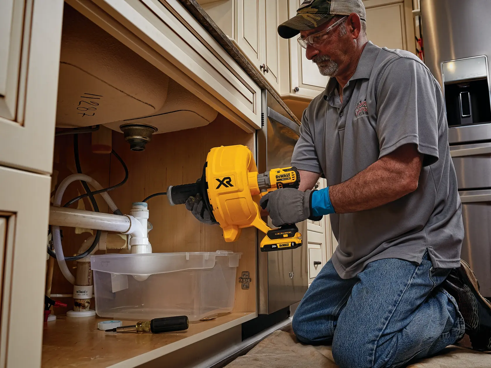 XR Brushless cordless drain snake is being used by a person to clear a pipe.