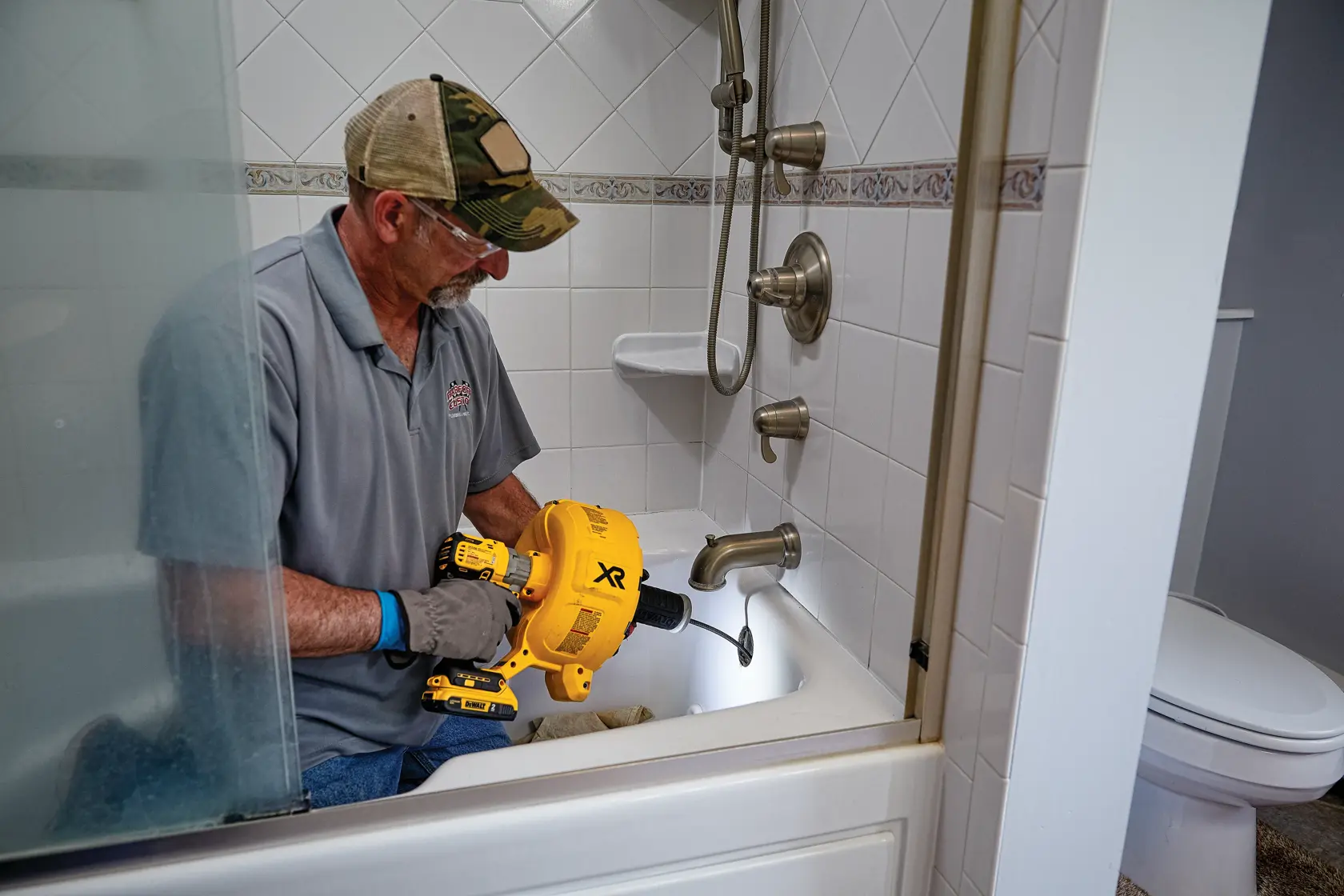 XR Brushless cordless drain snake is being used by a person to clear  drain from a bathtub.
