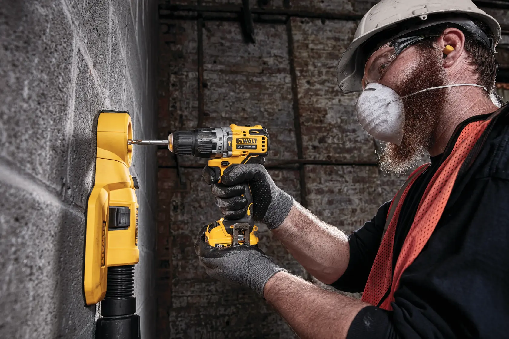 A person wearing gloves is using a yellow DEWALT cordless drill to drill into a concrete wall, next to a yellow device attached to the wall.