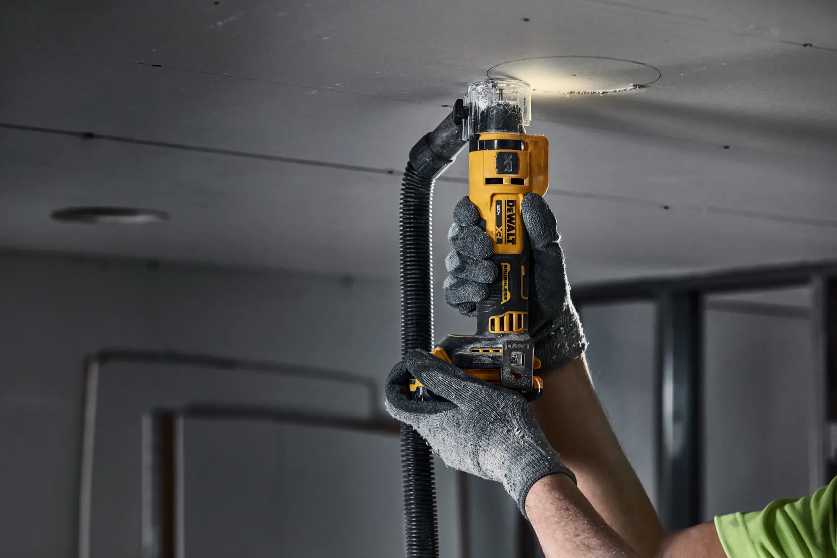 individual using a 20V MAX XR(®) Brushless Drywall Cutout Tool with dust extractor on ceiling
