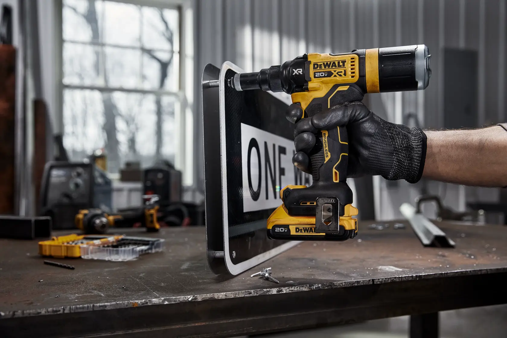 Person uses a DEWALT cordless drill on a metal sign in a workshop.