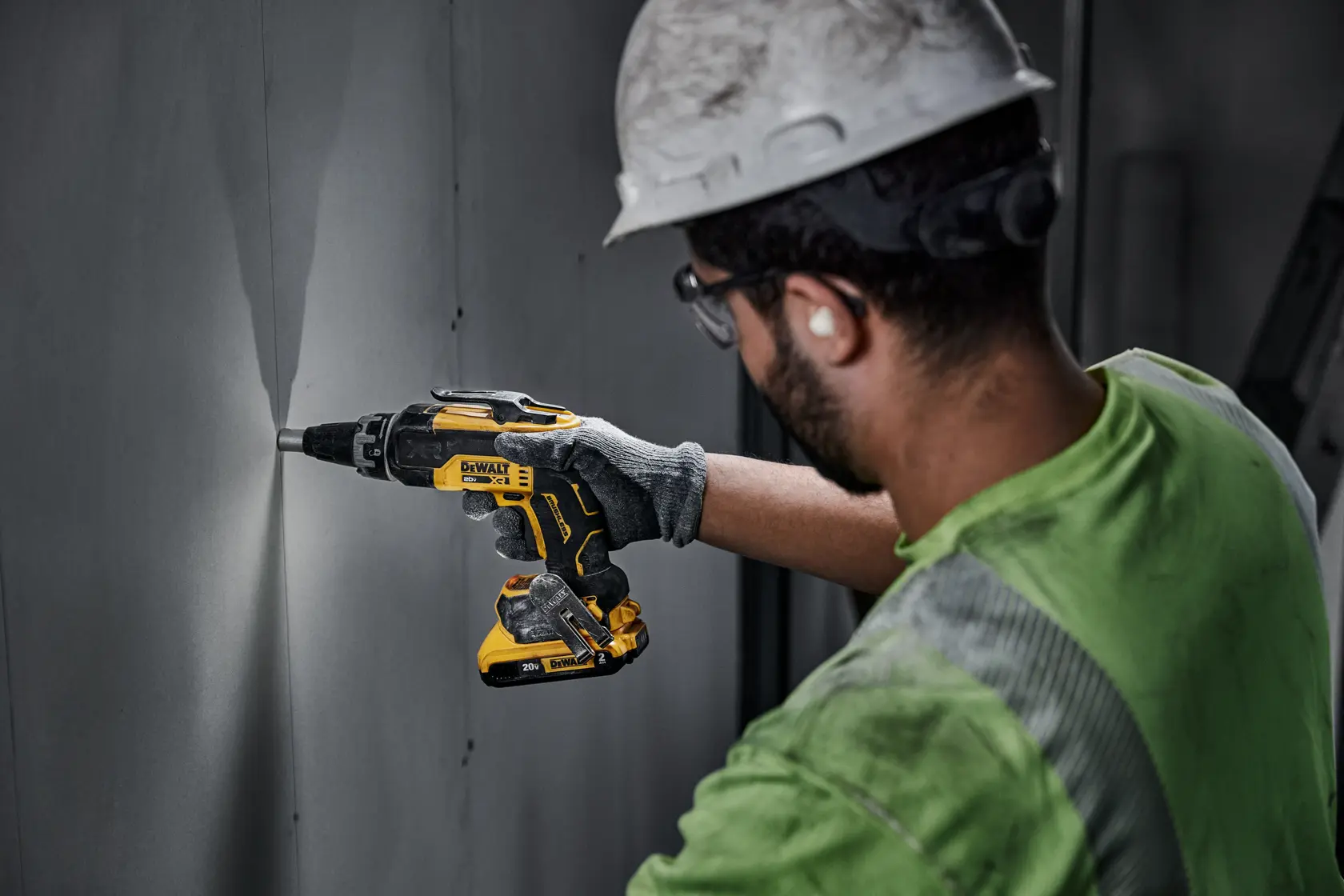 A person wearing a hard hat and gloves uses a DEWALT DCF630D2 cordless screwdriver to work on a wall panel indoors.