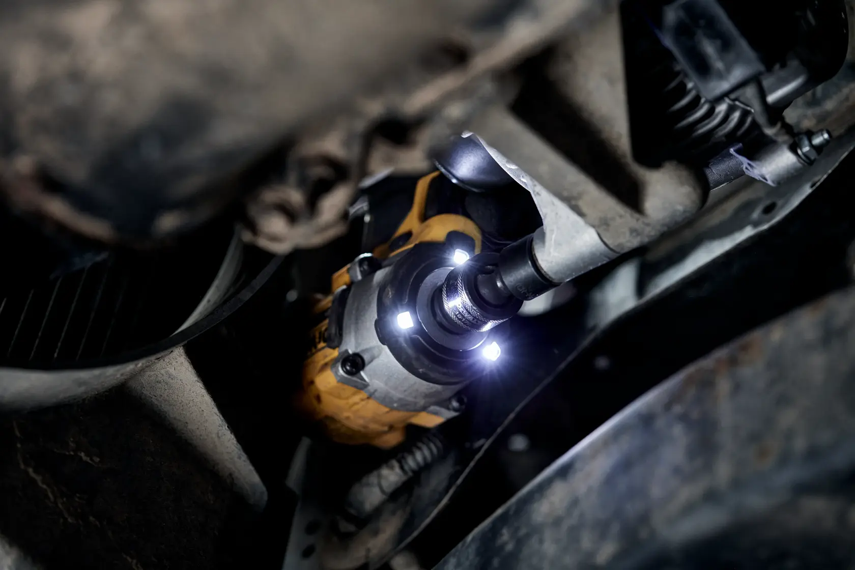 A close-up of a power tool, specifically an impact wrench with LED lights, being used to work on a vehicle's suspension or undercarriage.
