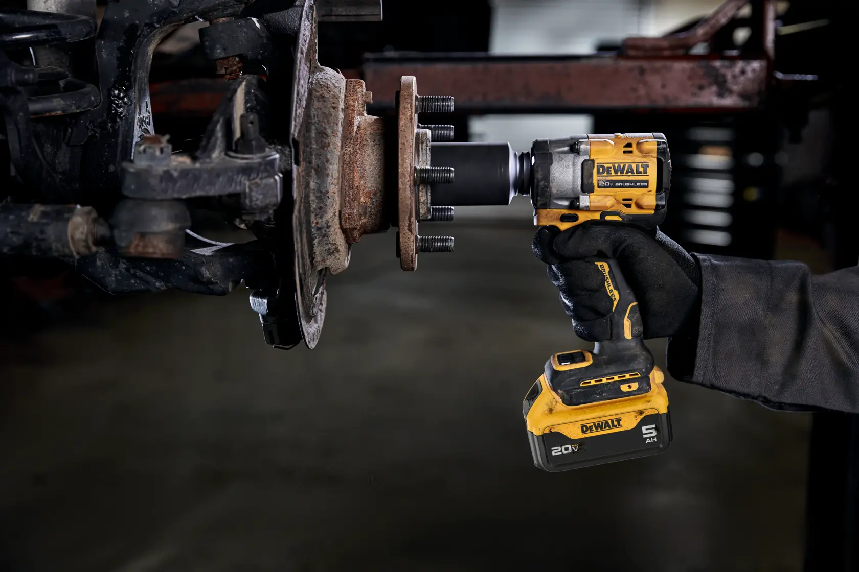 A person wearing a glove is using a yellow DEWALT cordless impact wrench to work on a rusty vehicle wheel hub in an automotive setting.