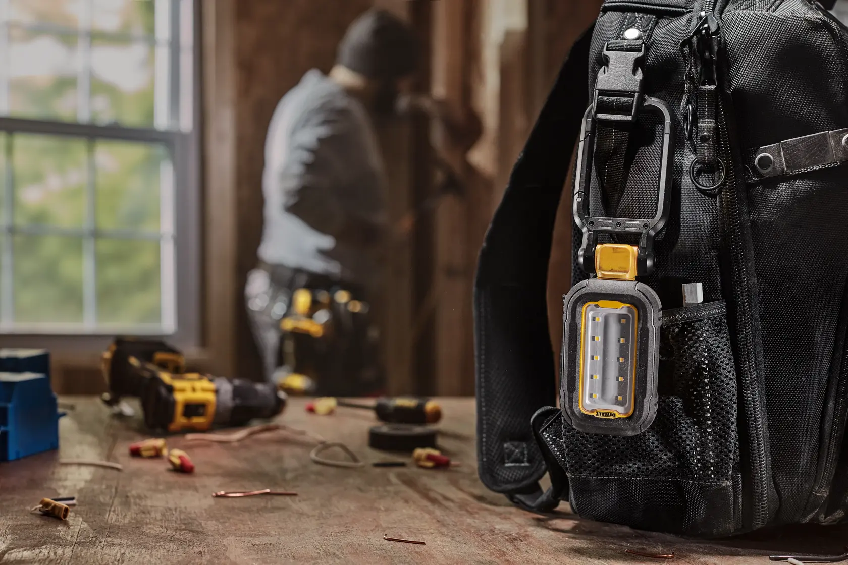 DEWALT task light attached to backpack using the hook feature while user works on something in the background 