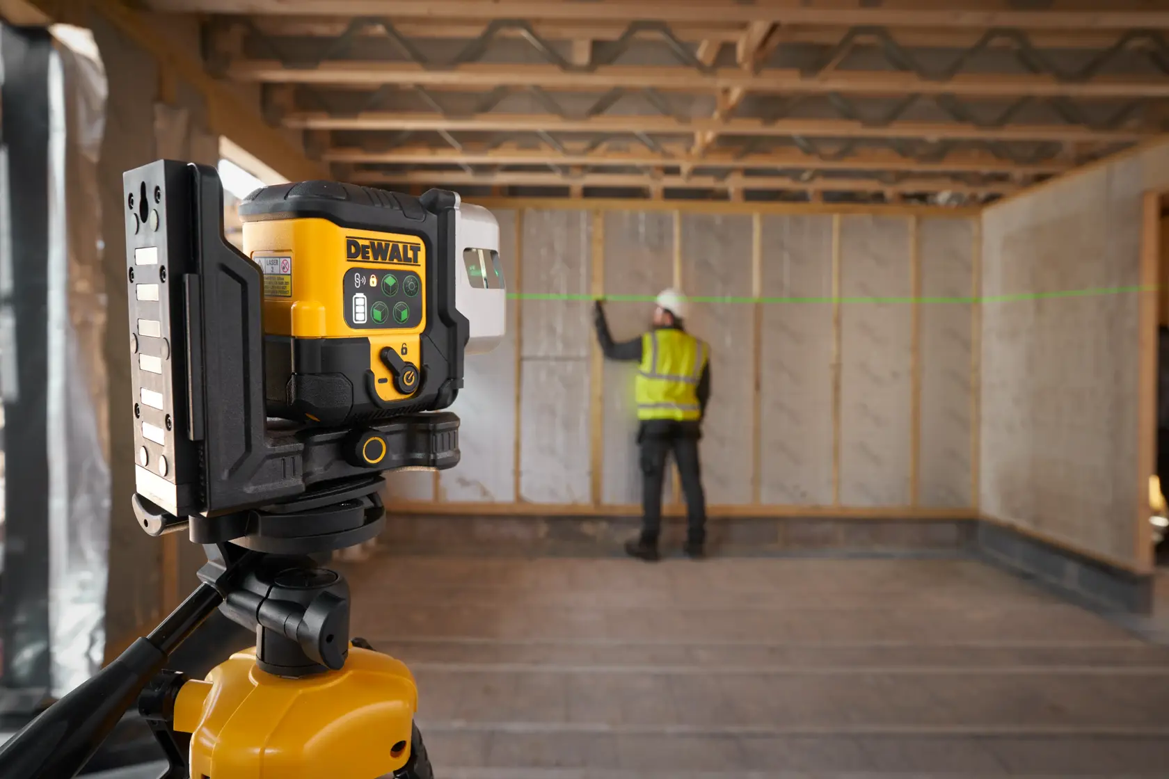 The DEWALT 3x 180 USB Green Beam Laser in foreground attached to tripod, green laser is on and worker is onsite in the background.