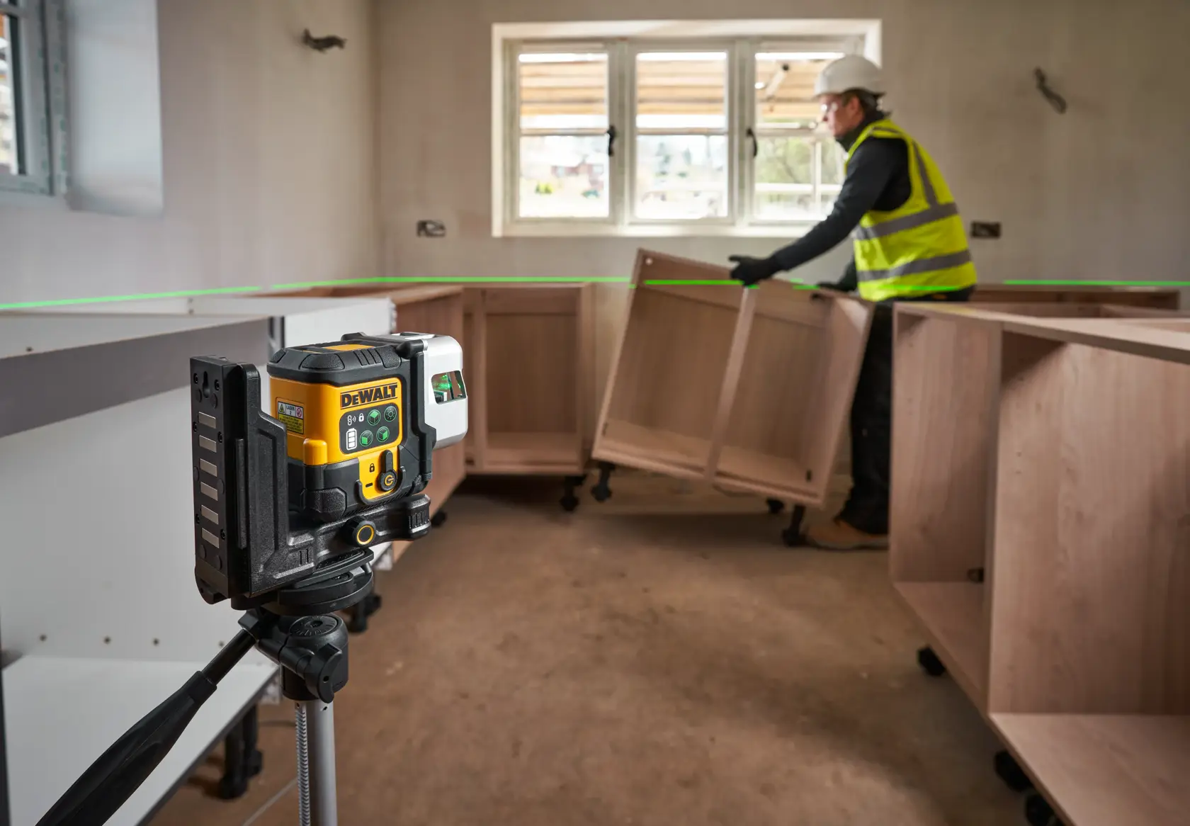 The DEWALT 3x 180 USB Green Beam Laser in foreground attached to tripod, helping to guide the worker on site fitting cabinets.