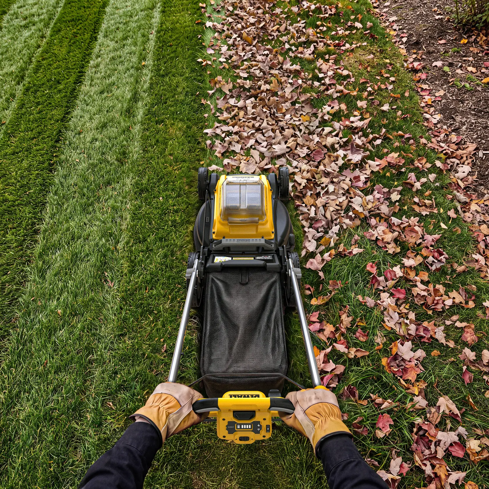 Hand inserting battery into yellow DEWALT lawn mower on grass.