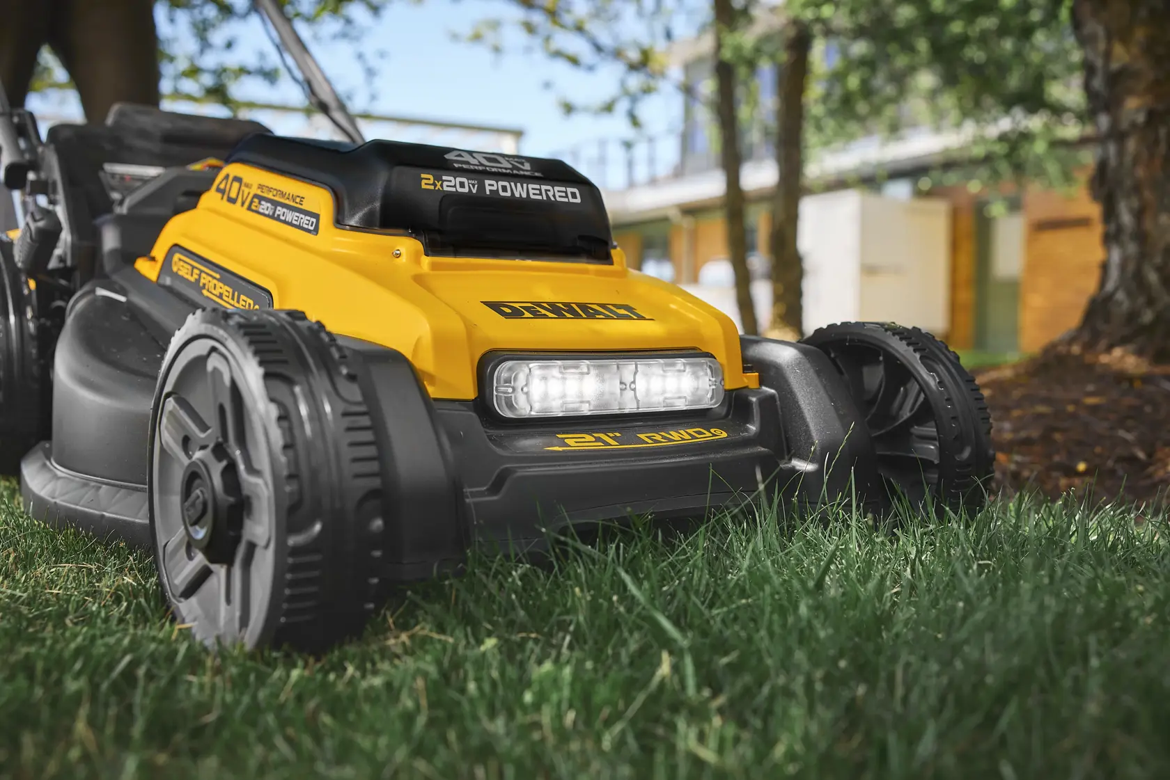 Yellow DEWALT electric lawn mower on grass, close-up showing wheels and headlight outdoors.