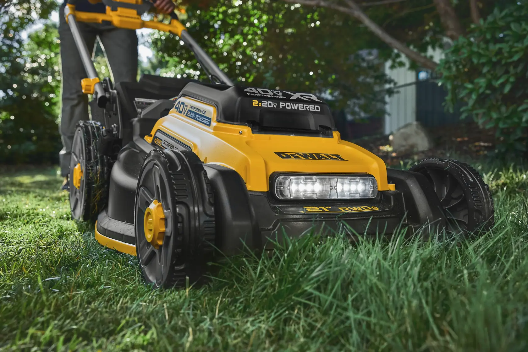 Yellow DEWALT lawn mower cutting grass outdoors, close-up view of wheels and LED lights.
