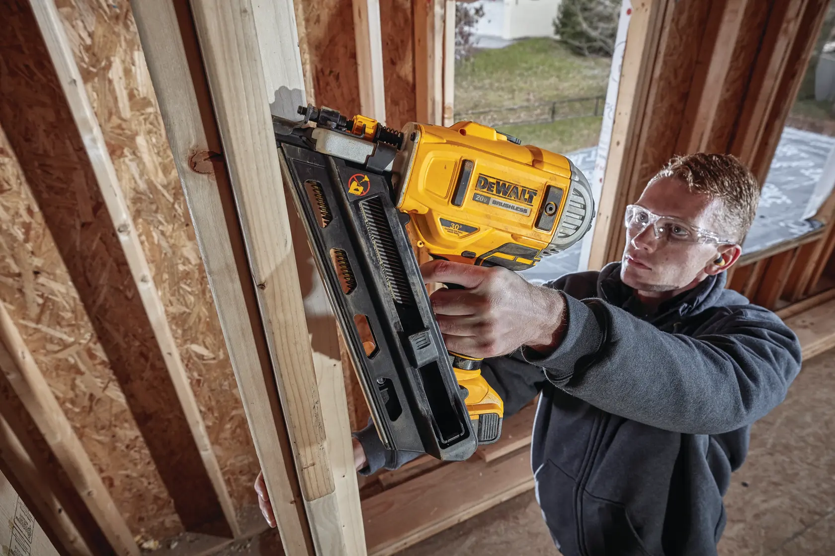 A person using a DEWALT cordless nail gun to fasten wooden beams in a building under construction. The user's face is blurred for privacy.