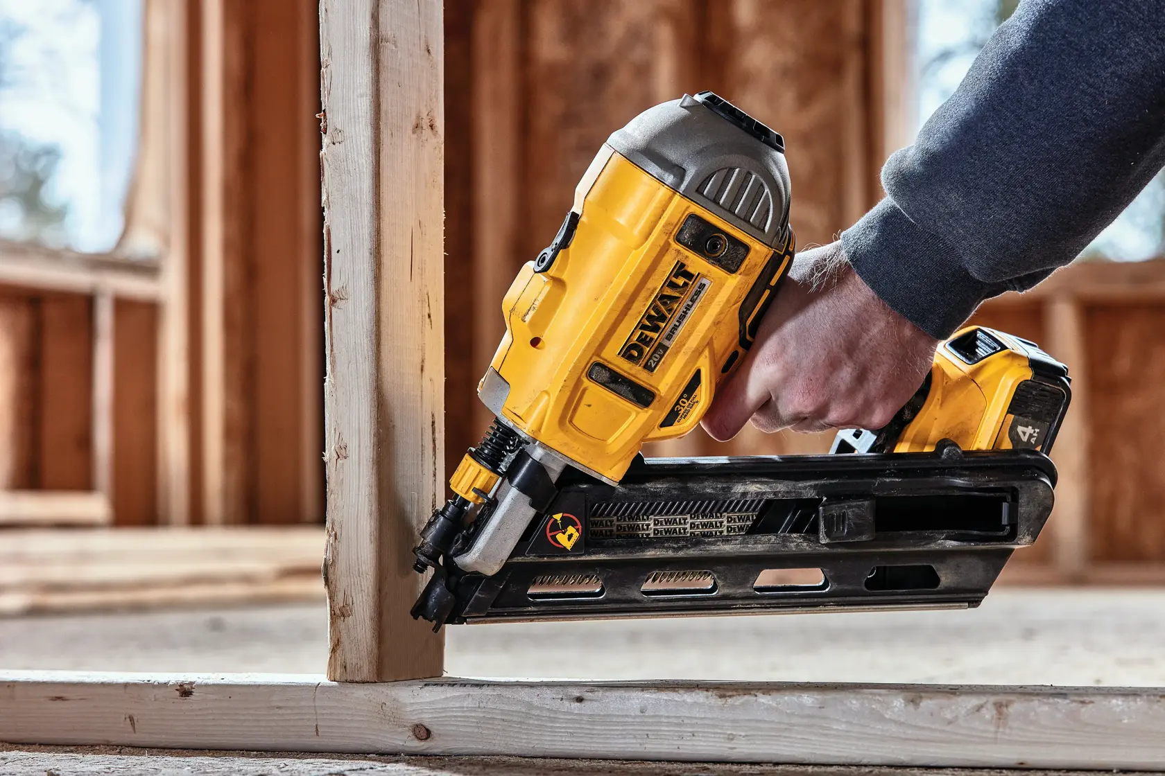 A person uses a DEWALT cordless nail gun to fasten a wooden frame during construction.
