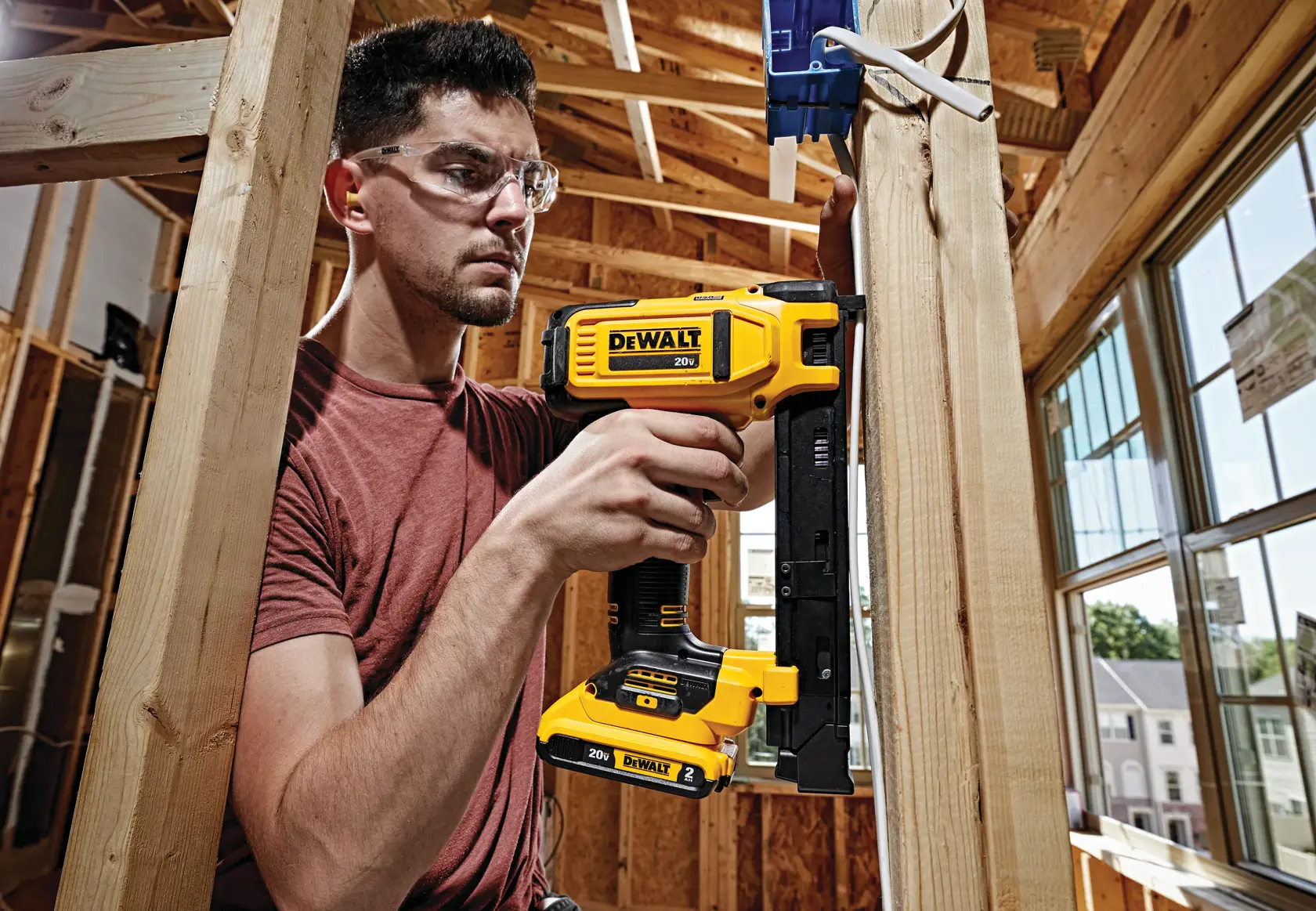 A person using a DEWALT 20V DCN701D1 cordless tool to fasten wiring during electrical work in a wooden framed room under construction. The focus is on the tool and the work process.
