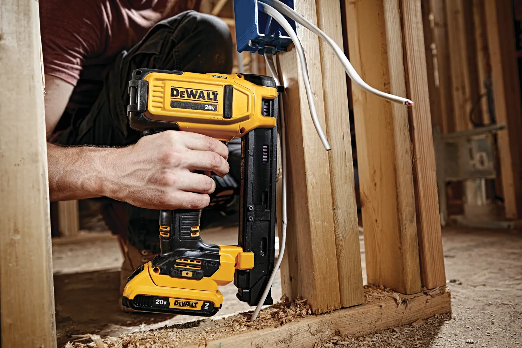 A person uses a DEWALT 20V cordless cable stapler to secure electrical wires to wooden framing during construction.