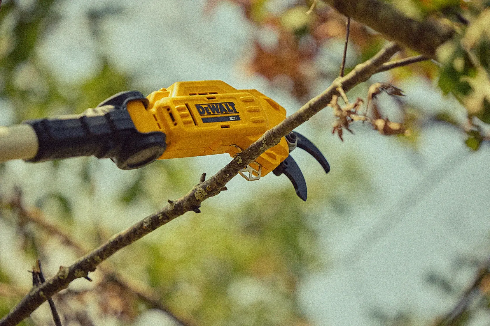 A DEWALT cordless pruner is being used to cut a tree branch outdoors.