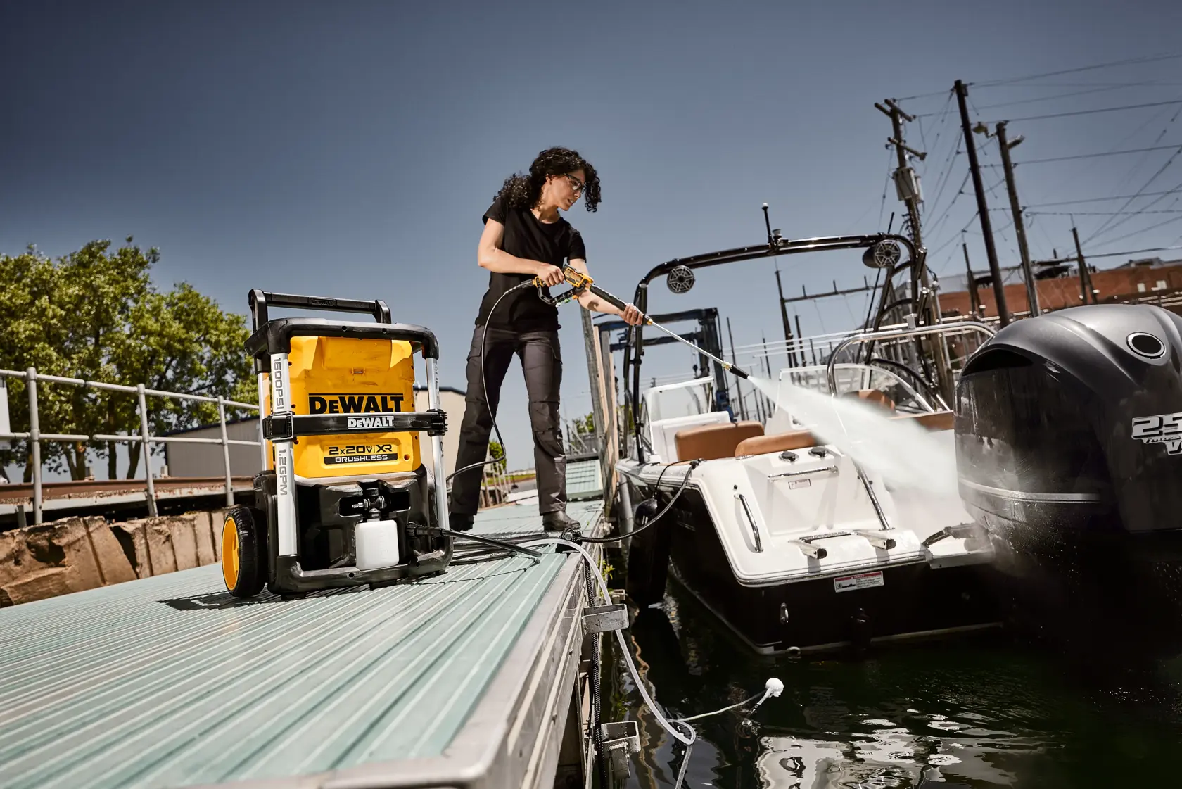 A person uses a yellow DEWALT pressure washer to clean the back of a boat while standing on a dock.
