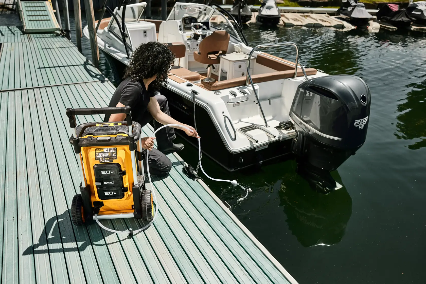 A person uses a yellow DEWALT portable pressure washer on a dock next to a boat, with the pressure washer hose submerged in the water.