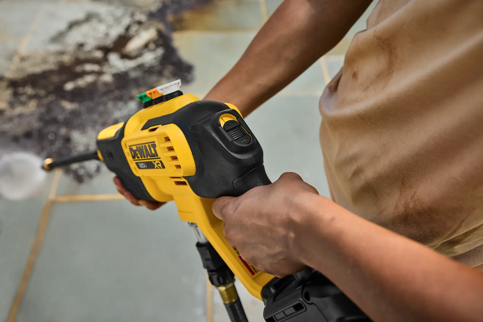 Person using a DeWalt cordless power washer to clean dirty tiles outdoors.