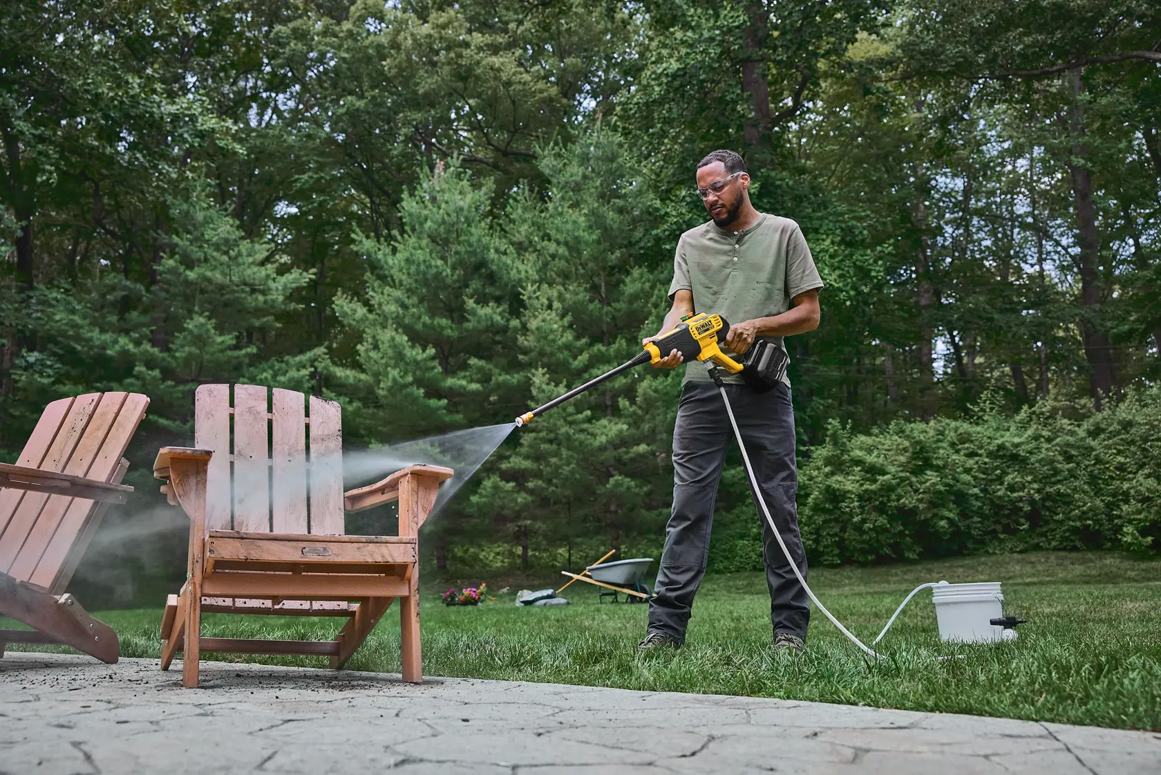 Person cleaning an outdoor wooden chair with a DEWALT power washer in a backyard setting.