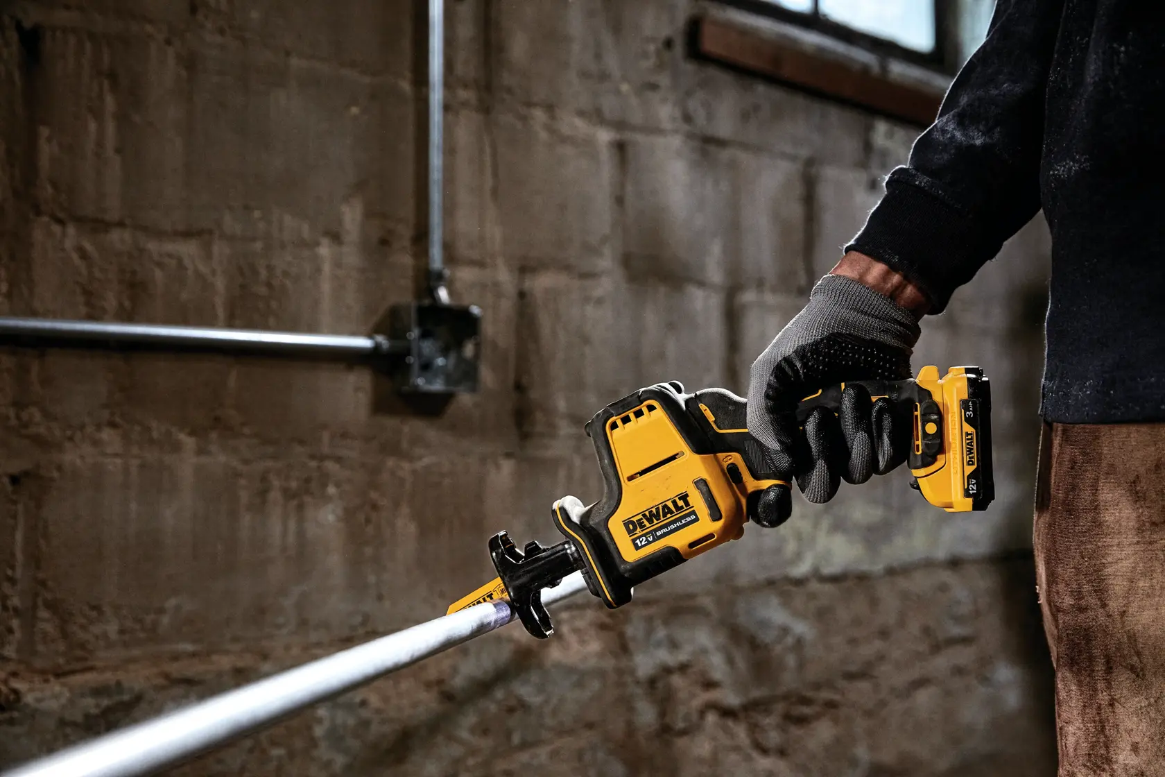 Person wearing work gloves using a DEWALT cordless reciprocating saw to cut a metal pipe in an industrial setting.