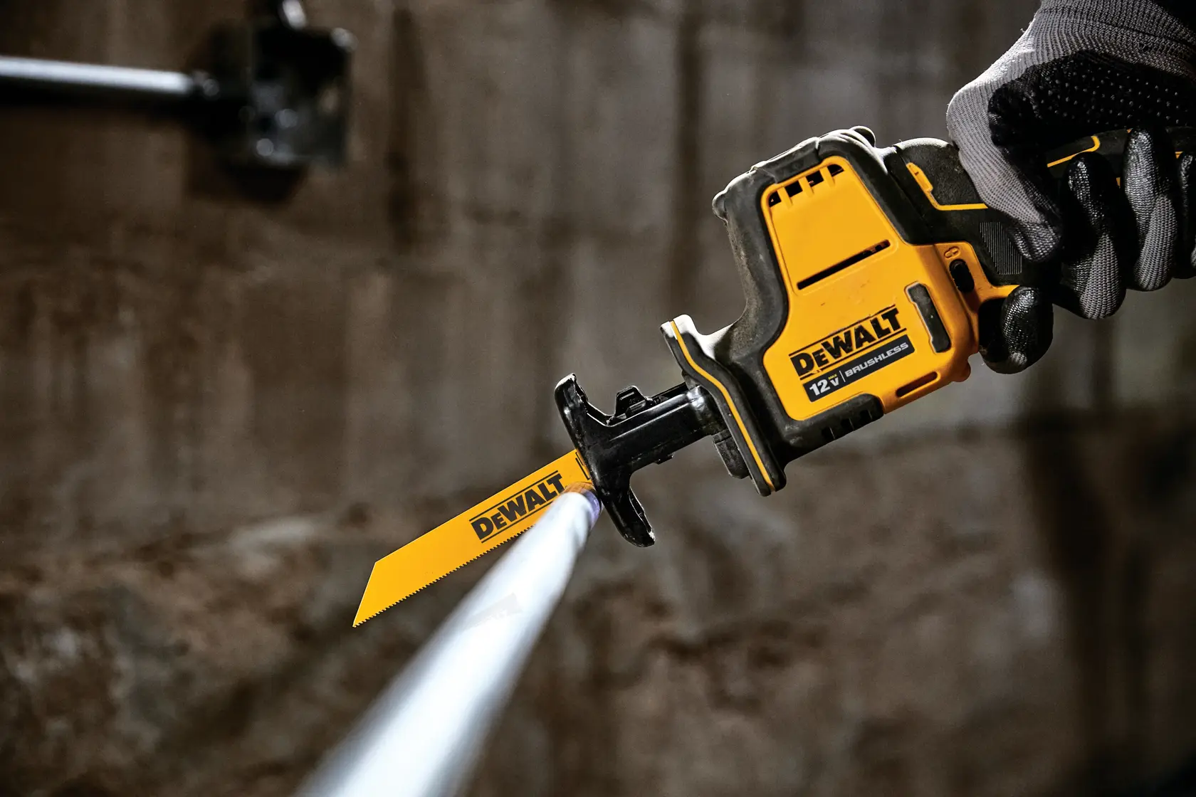 A DEWALT 12V reciprocating saw being used to cut a metal pipe, held by a gloved hand in an industrial setting.