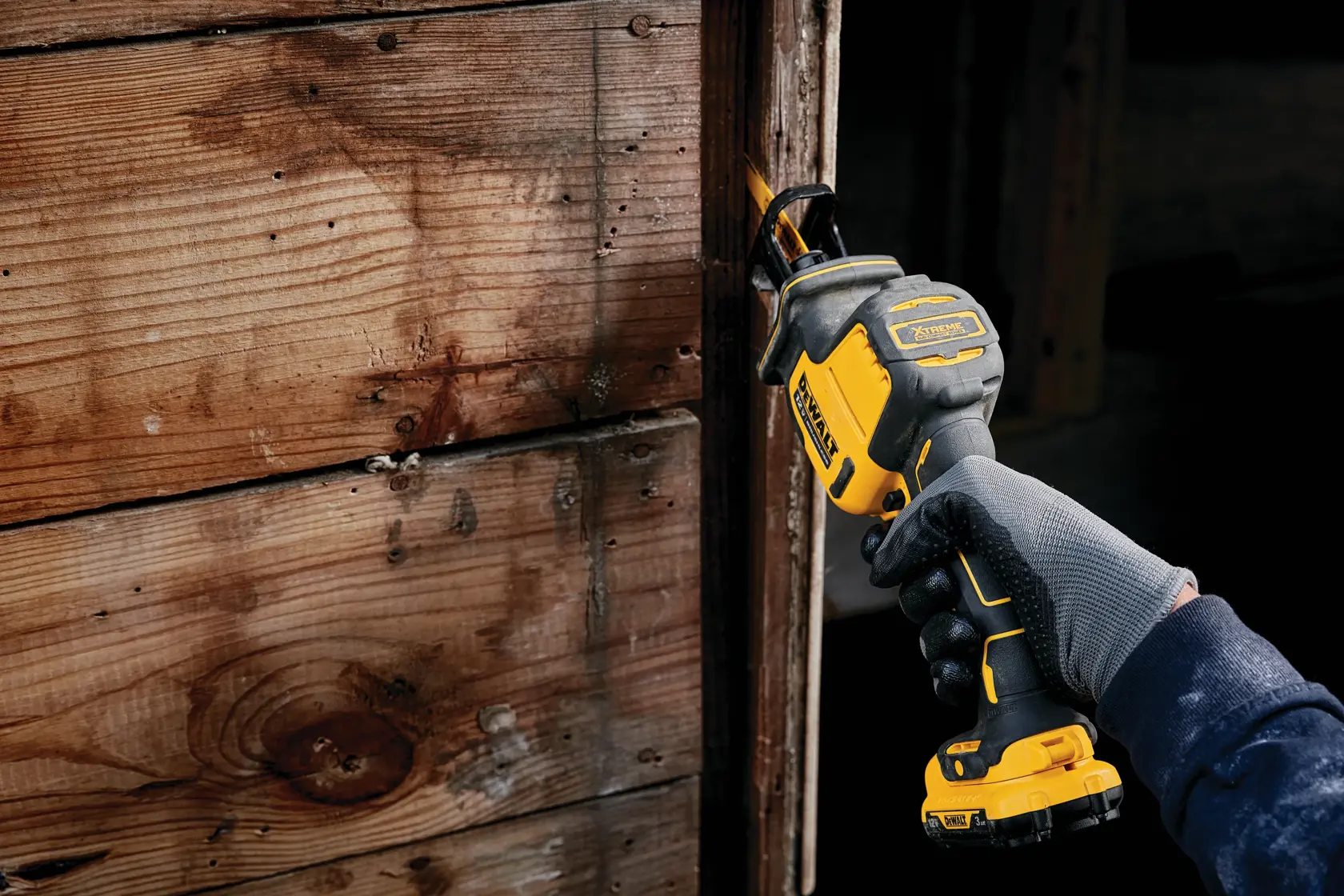 A person wearing a glove is using a DEWALT cordless reciprocating saw to cut through wooden boards.