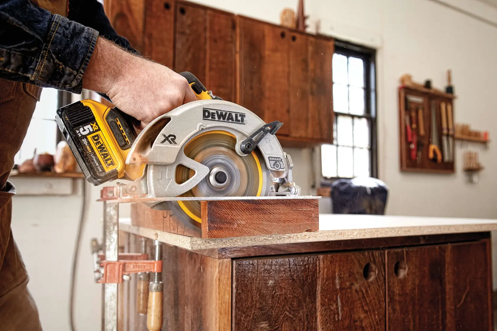 A person using a DEWALT cordless circular saw to cut a piece of wood in a workshop setting.