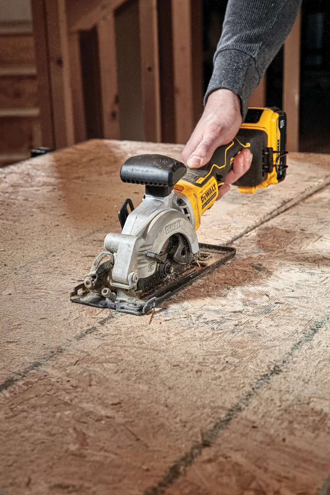 A person using a DEWALT cordless circular saw to cut a sheet of wood on a workbench.